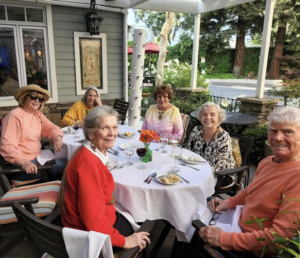 Posing for a photo are senior sitting at a dining table outside