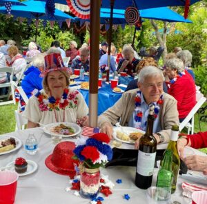 Seniors sitting outside eating food at a table celebrating the 4th of July and drinking wine
