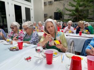 Seniors painting at a table outside while drinking wine