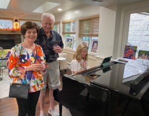 Younger girl singing and playing a piano while two seniors listen