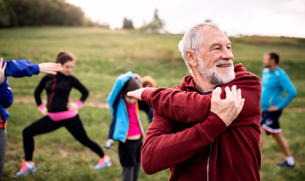 A large group of fit and active seniors doing exercise in nature, stretching.